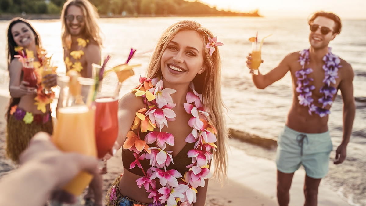 Cheers! Group of young attractive friends are having fun on beach, drinking cocktails and smiling. Party in Hawaiian style.