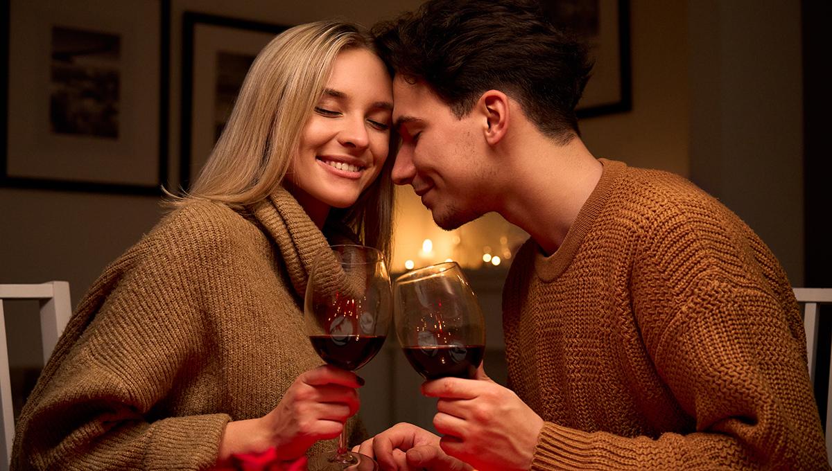 Happy couple in love clinking glasses drinking red wine having romantic dinner.